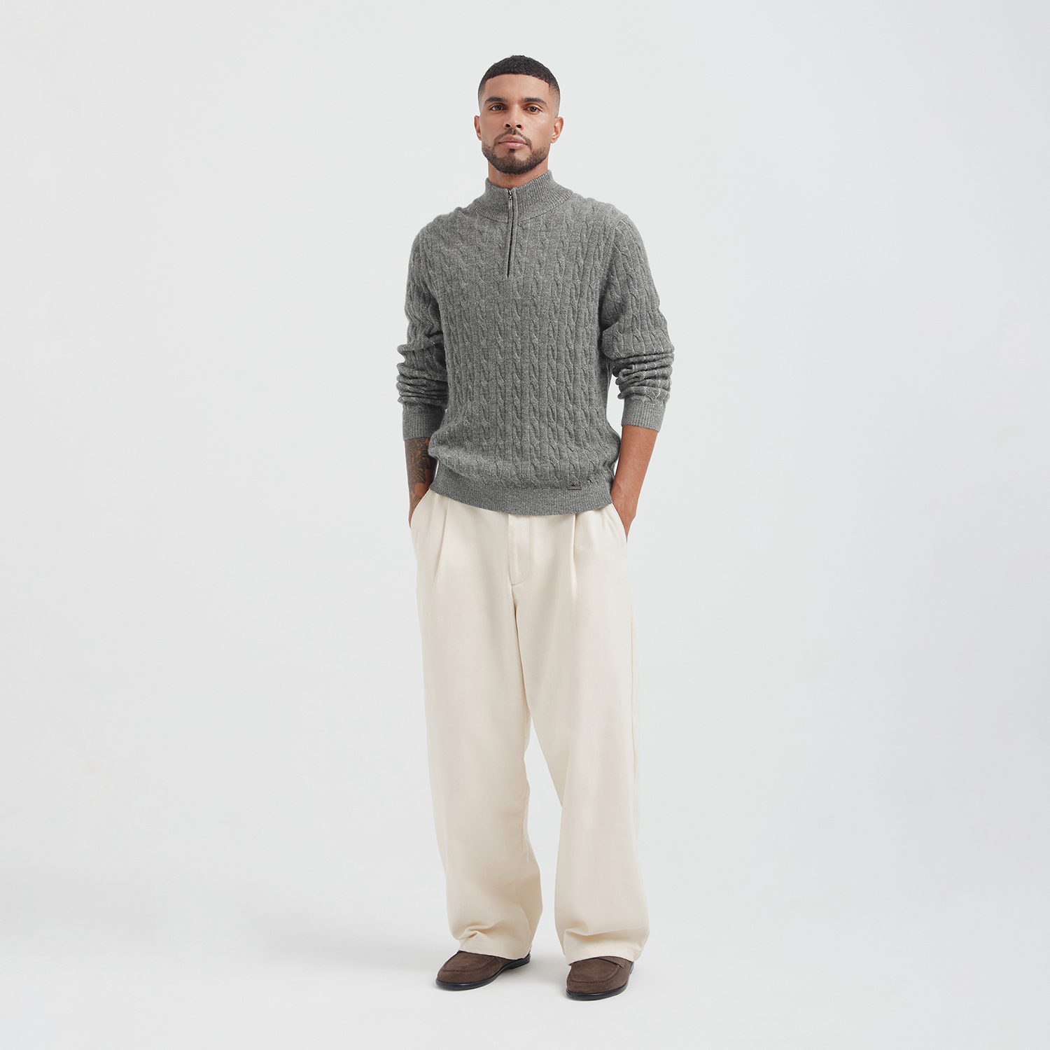 Man wearing a gray cable knit sweater and beige pants on a white background