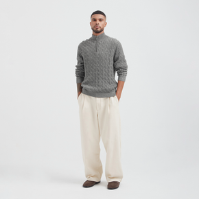 Man wearing a gray cable knit sweater and beige pants on a white background