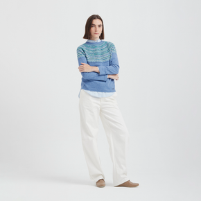 Woman wearing a blue striped sweater and white pants on a light gray background