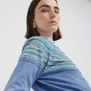 Woman wearing a blue sweater with a patterned sleeve on a white background