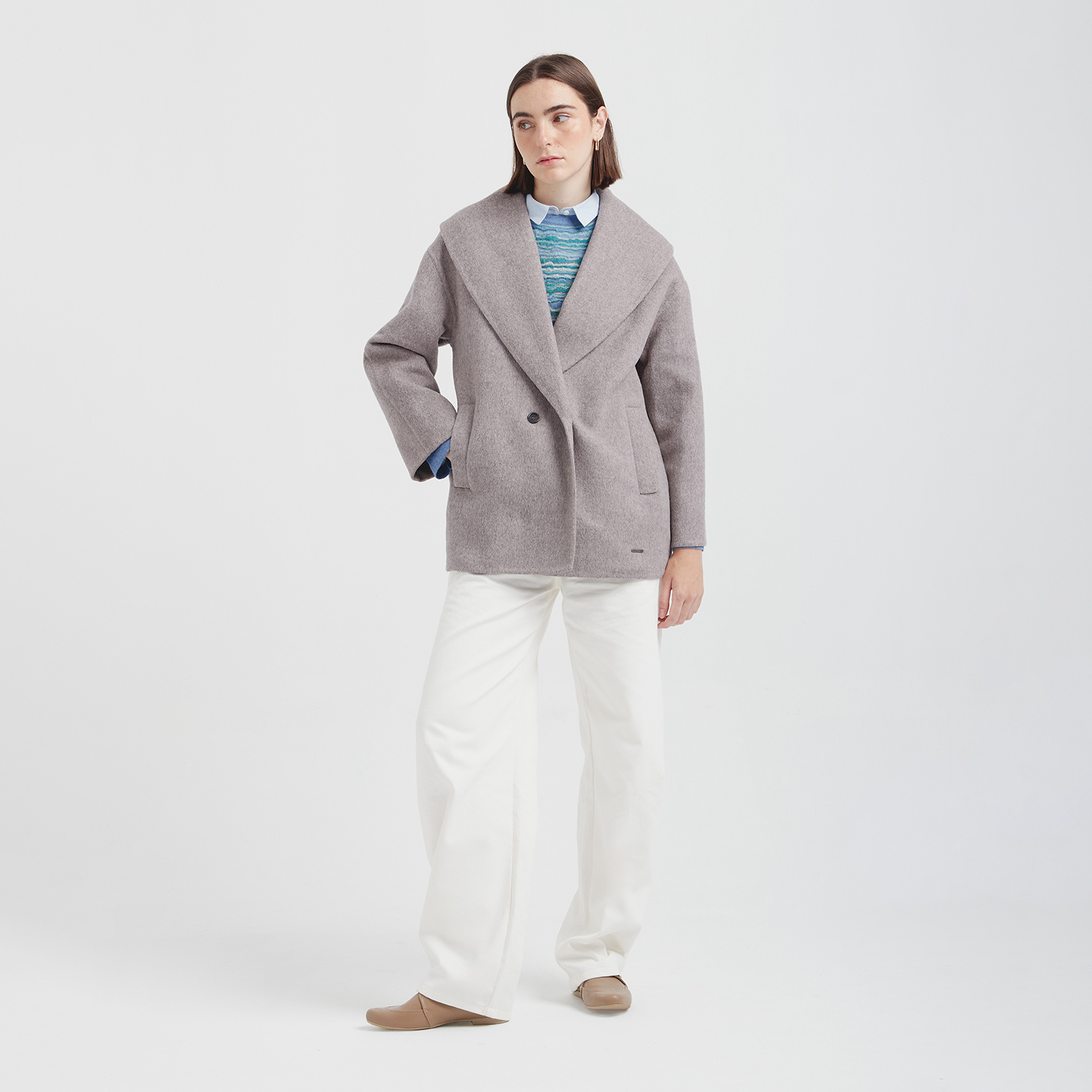 Person wearing a gray coat, blue shirt, white pants, and brown shoes on a white background