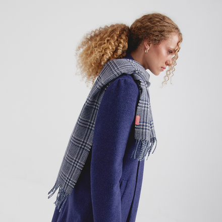 Woman wearing a blue coat and plaid scarf on a plain background
