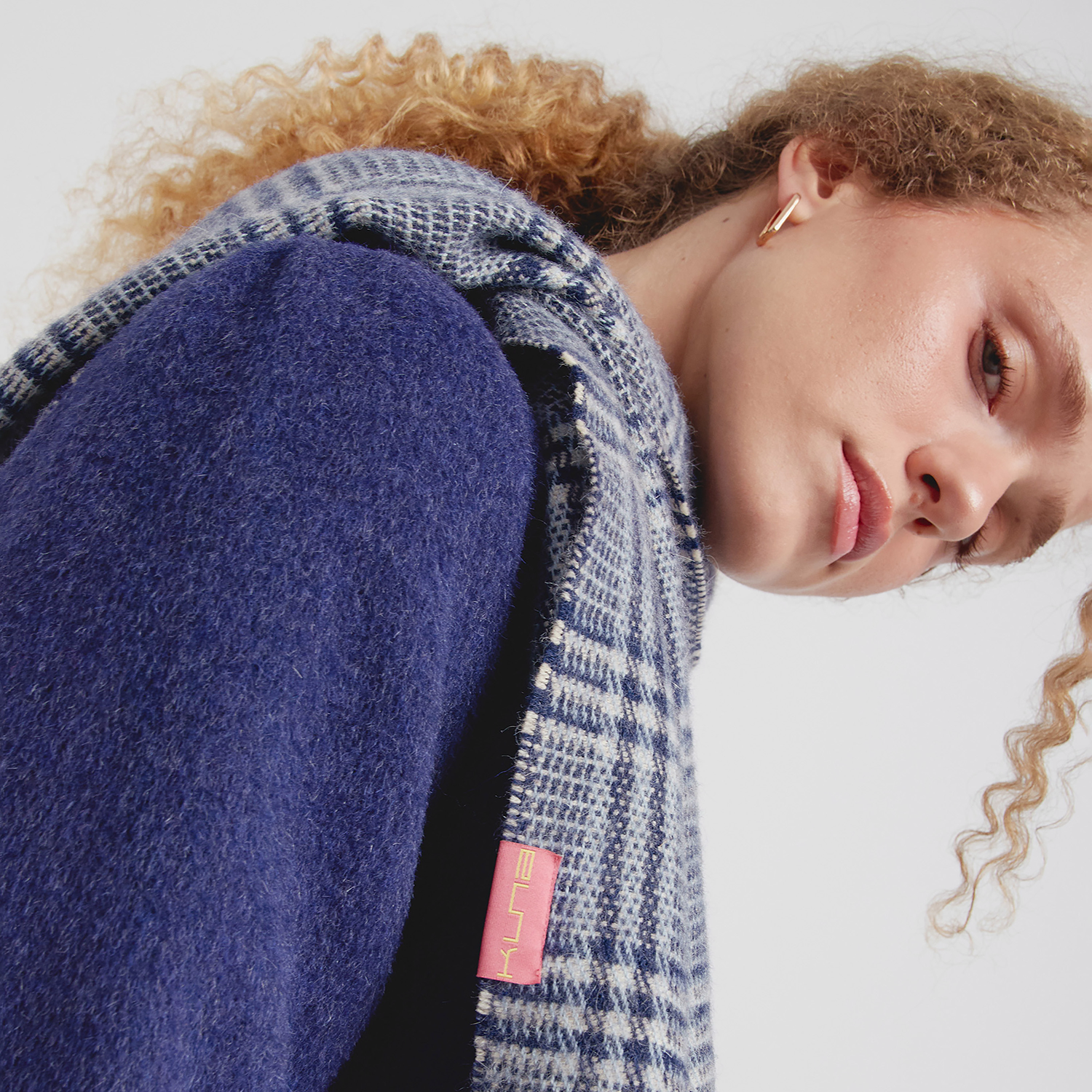 Person wearing a blue and gray patterned scarf with a visible brand logo on a white background