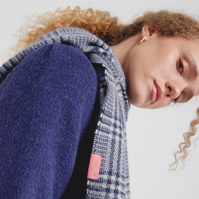 Person wearing a blue and gray patterned scarf with a visible brand logo on a white background