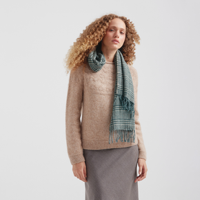 Woman wearing a beige sweater and plaid scarf on a plain background
