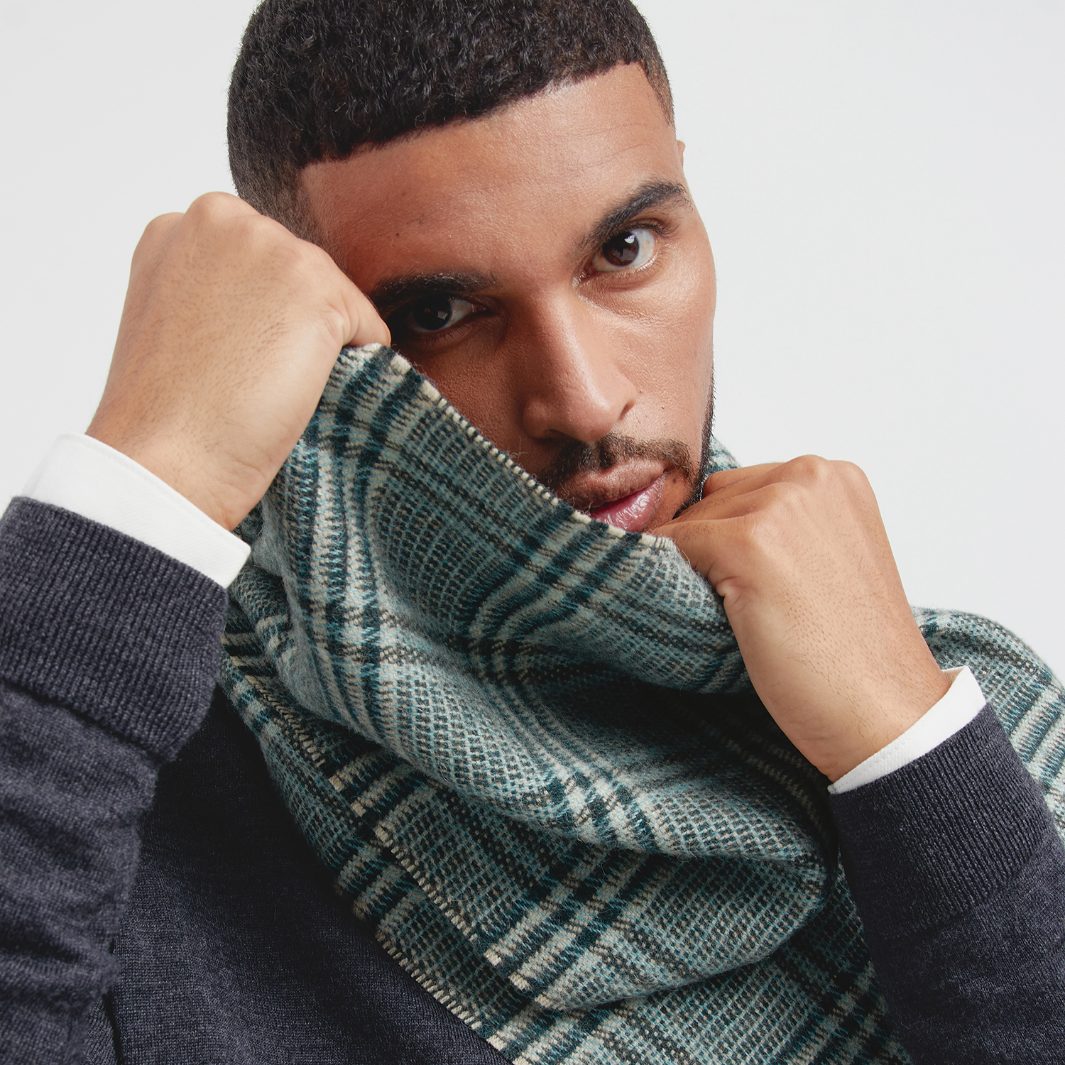 Man wearing a green plaid scarf with a neutral background