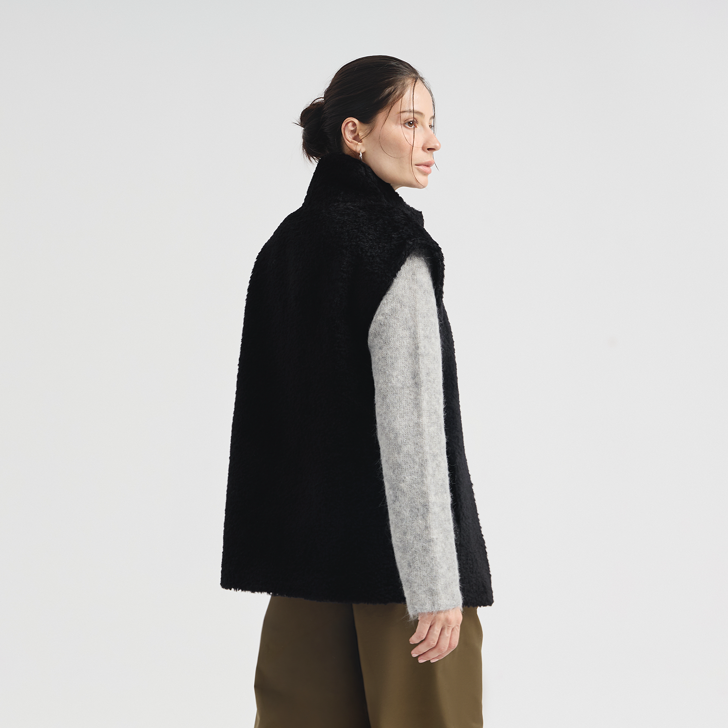 Woman wearing a black vest over a gray shirt on a white background