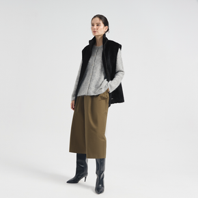 Woman wearing a black vest, gray sweater, brown skirt, and black boots on a white background