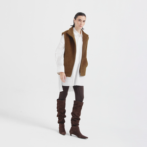 Woman wearing a brown vest, white shirt, and brown knee-high boots on a white background