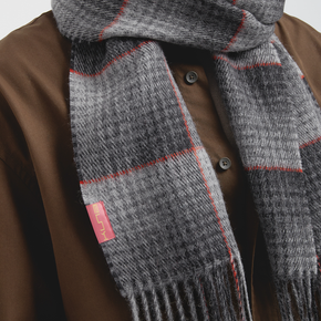Gray scarf with red accents worn over a brown jacket on a neutral background