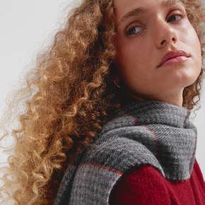 Woman wearing a gray scarf and red top against a light background