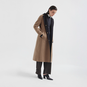 Person wearing a long beige coat over a black outfit on a white background