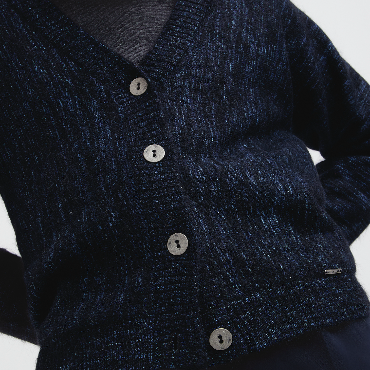 Close-up of a dark blue textured cardigan with buttons on a white background