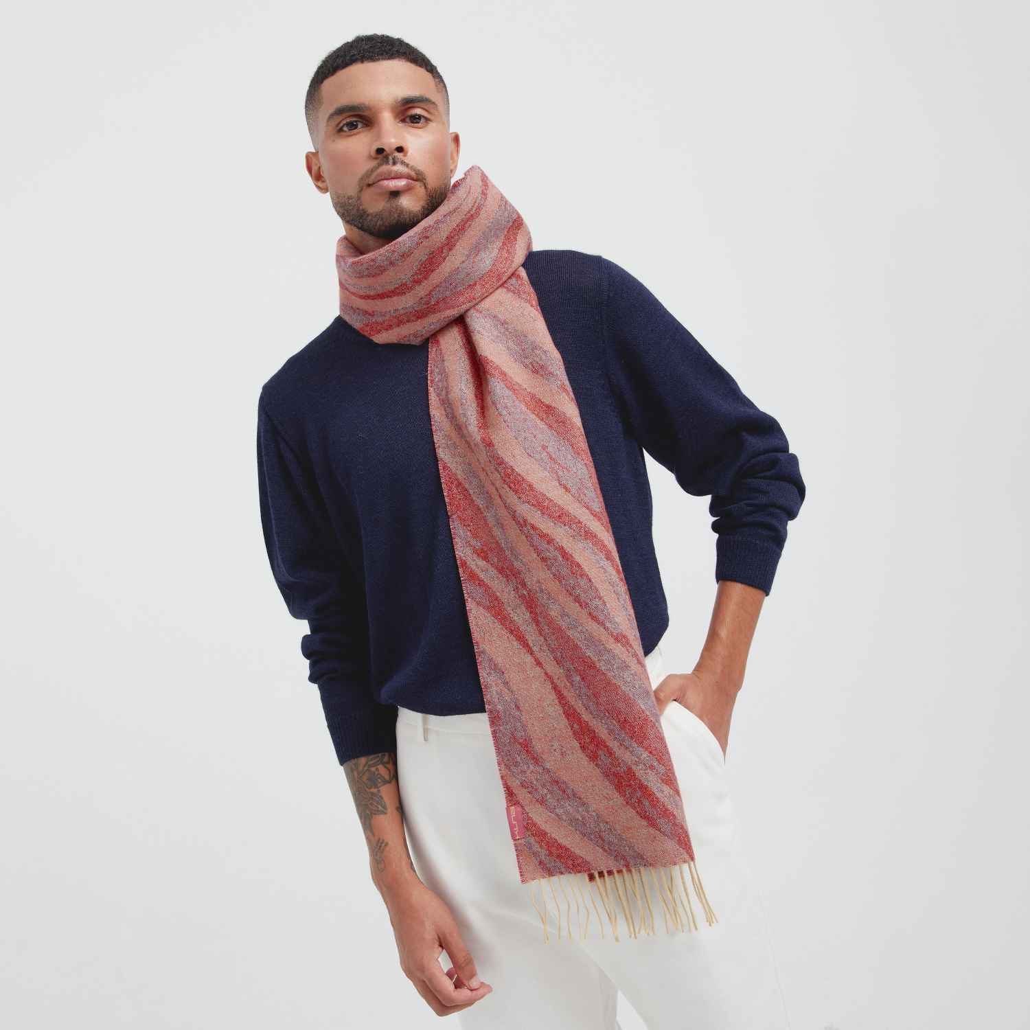 Man wearing a navy sweater and pink striped scarf on a white background
