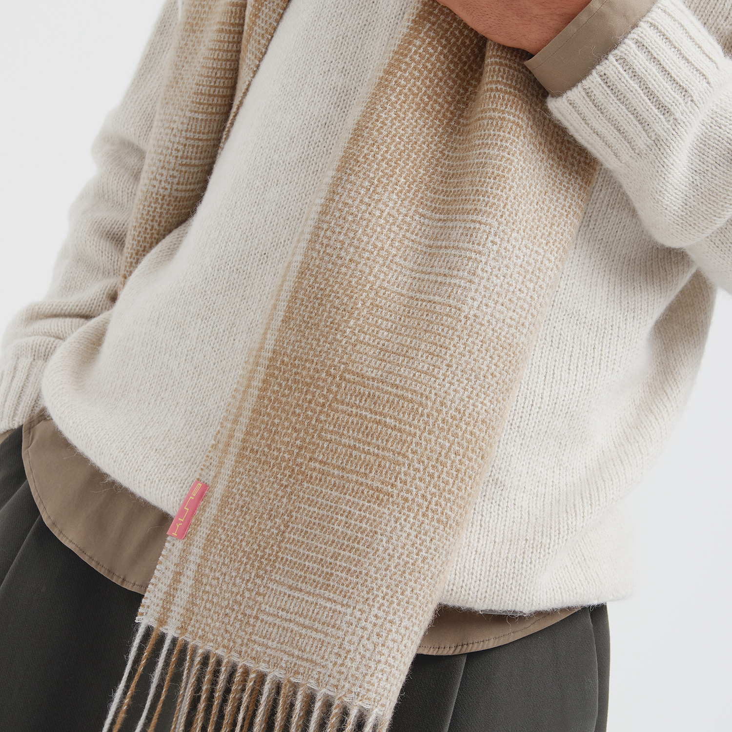 Person wearing a beige sweater and scarf with a white background