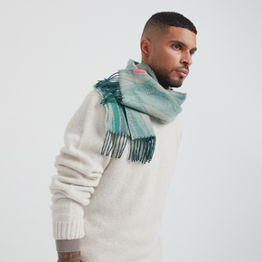 Man wearing a white sweater and green scarf on a light gray background