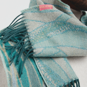 Teal and gray patterned scarf with fringes and a visible brand label on a light background