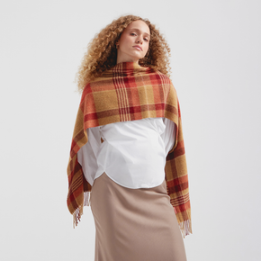 Woman wearing a plaid scarf over a white shirt and beige skirt on a light gray background