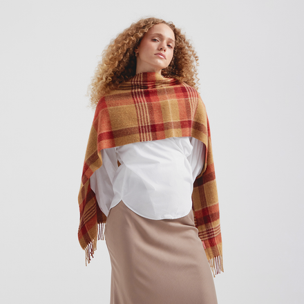 Woman wearing a plaid scarf over a white shirt and beige skirt on a light gray background