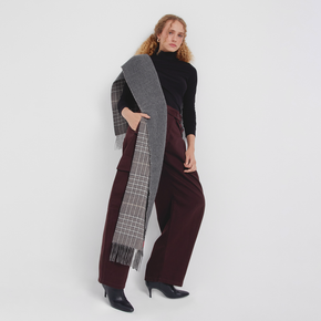 Woman wearing a long plaid scarf, black turtleneck, and burgundy pants on a white background