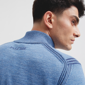 Man wearing a blue sweater with a brand logo on a light gray background