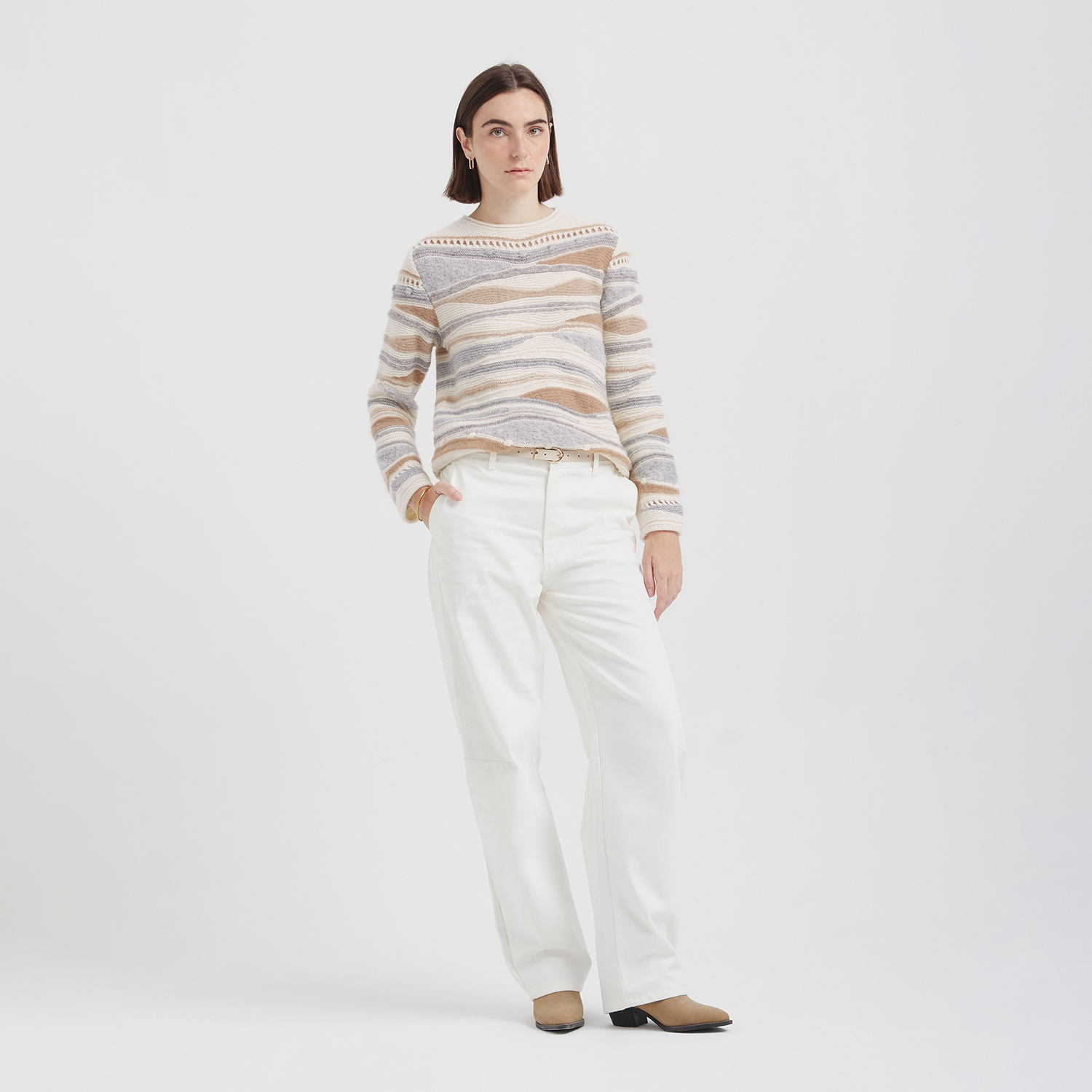 Woman wearing a striped sweater and white pants on a white background