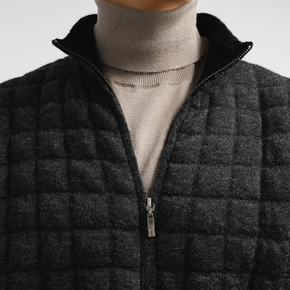 Dark quilted jacket with a zipper on a neutral background