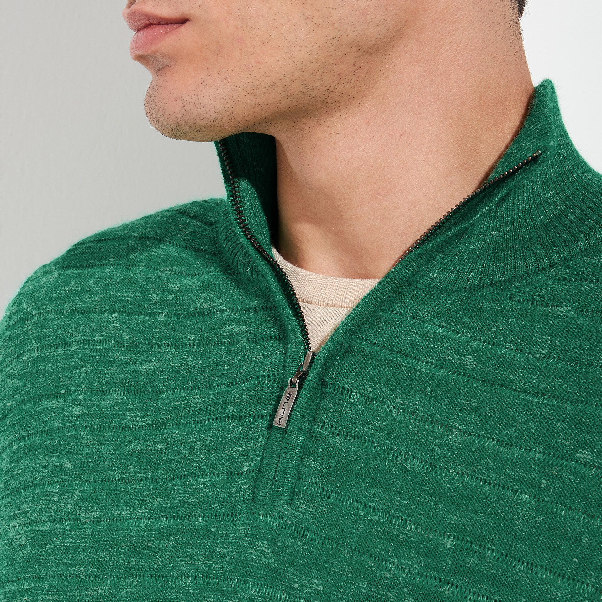 Close-up of a person wearing a green zip-up sweater against a gray background