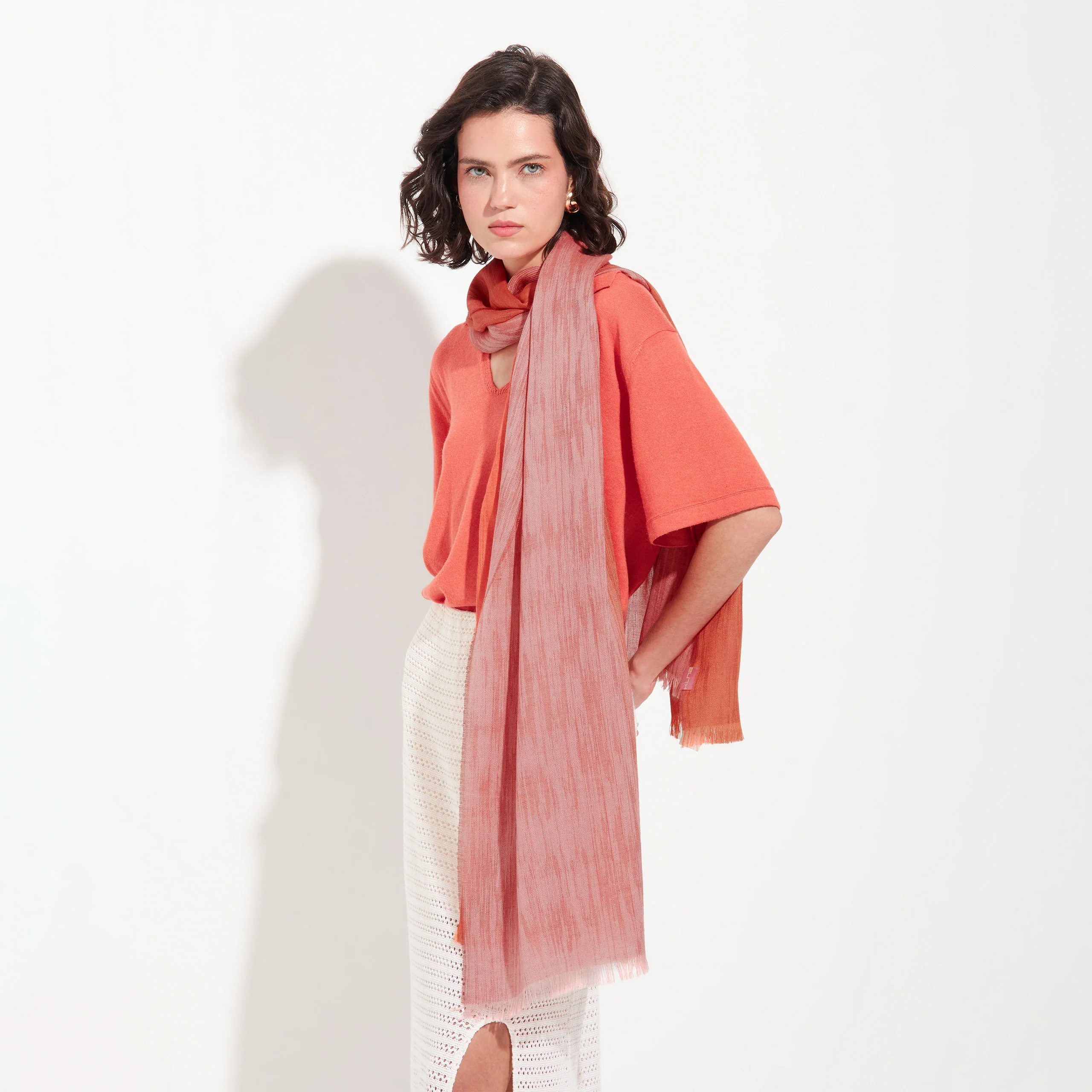 Woman wearing a coral blouse and pink scarf on a white background