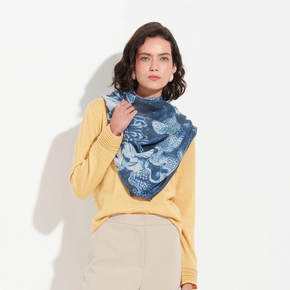 Woman wearing a yellow sweater and blue patterned scarf against a white background