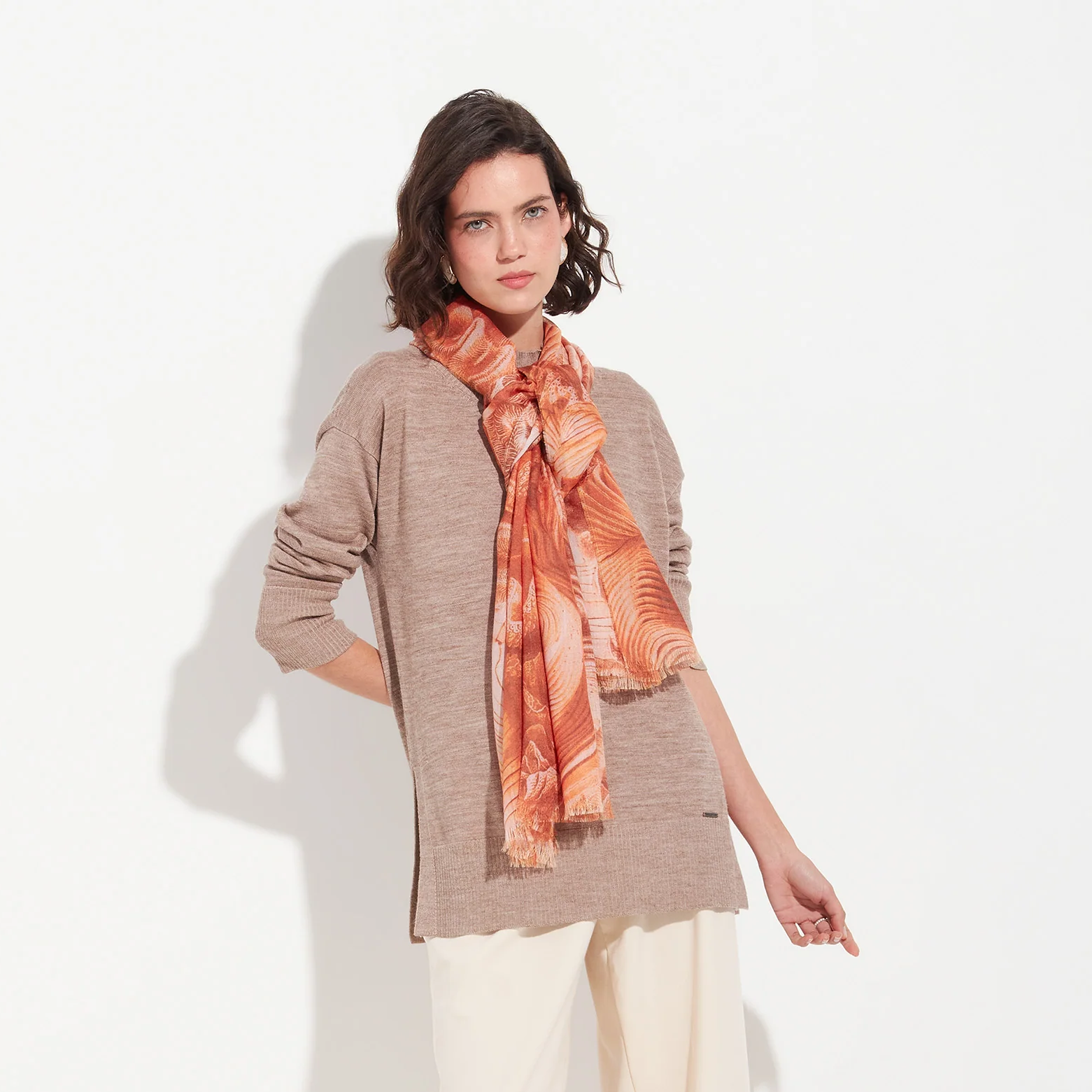 Woman wearing a beige sweater and orange scarf on a white background