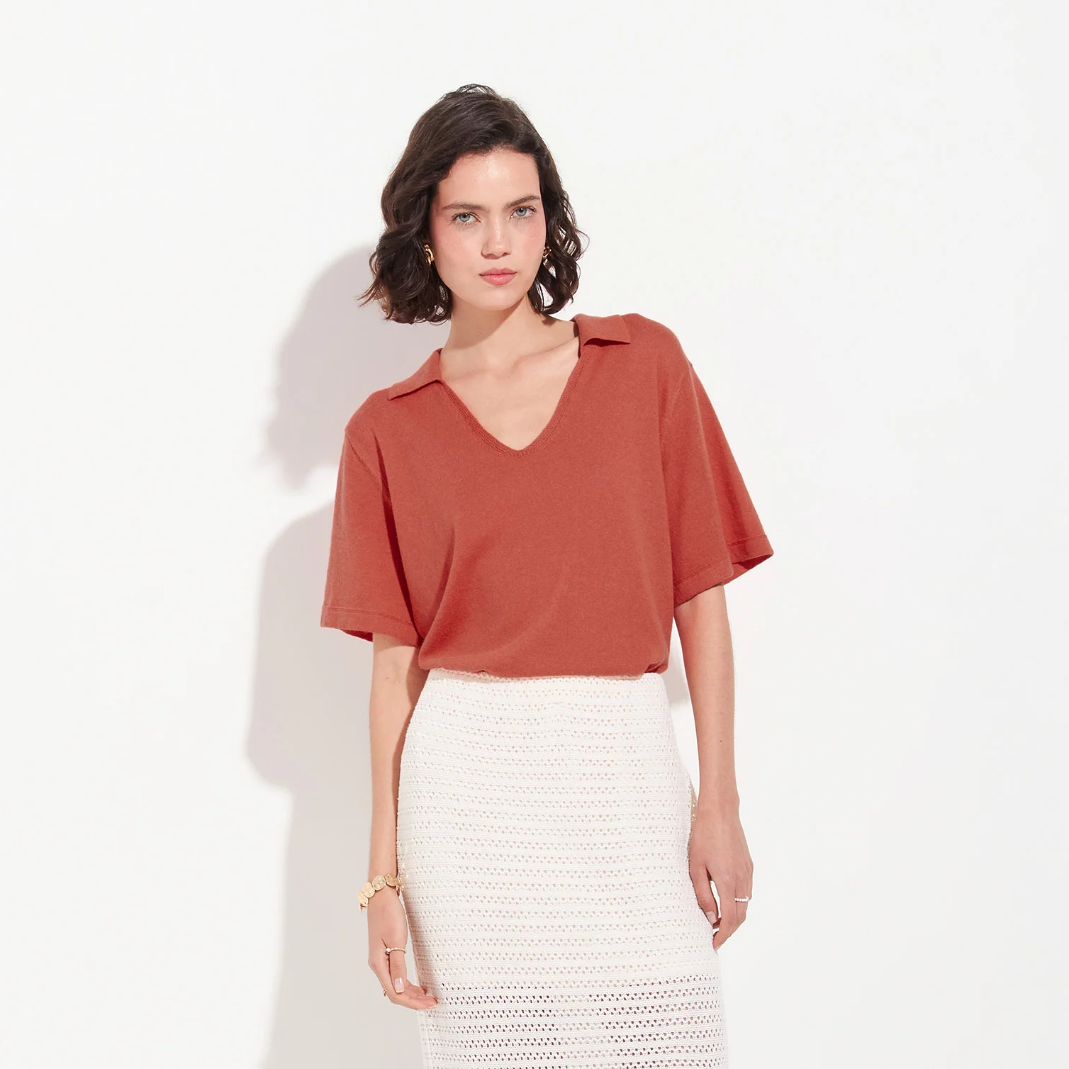 Woman wearing a rust-colored top and white skirt on a white background