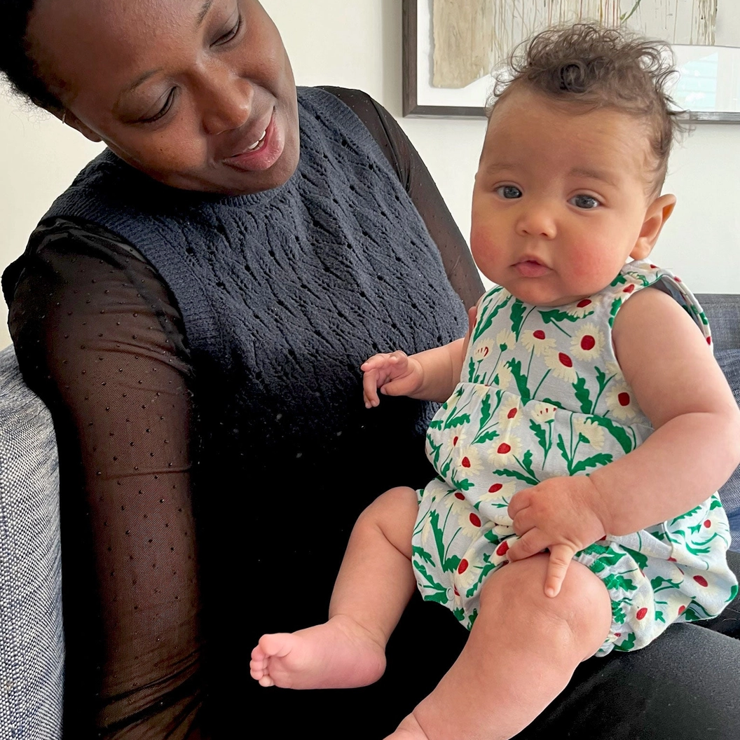 Woman holding a baby in a floral romper in a home setting