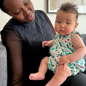 Woman holding a baby in a floral romper in a home setting