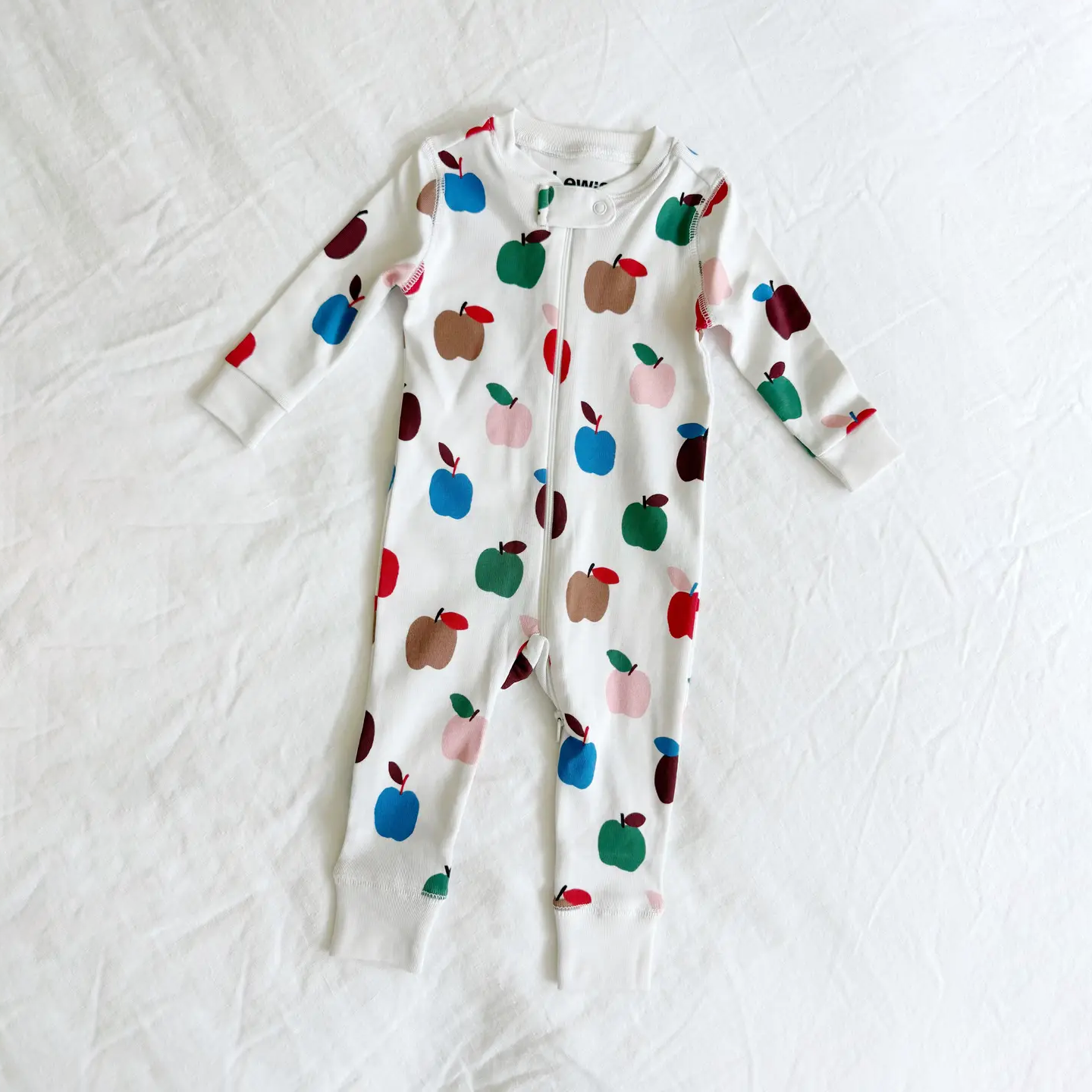 A baby long-sleeve footless sleeper with a white base and an all-over colorful apple print, laid flat on a white fabric background.