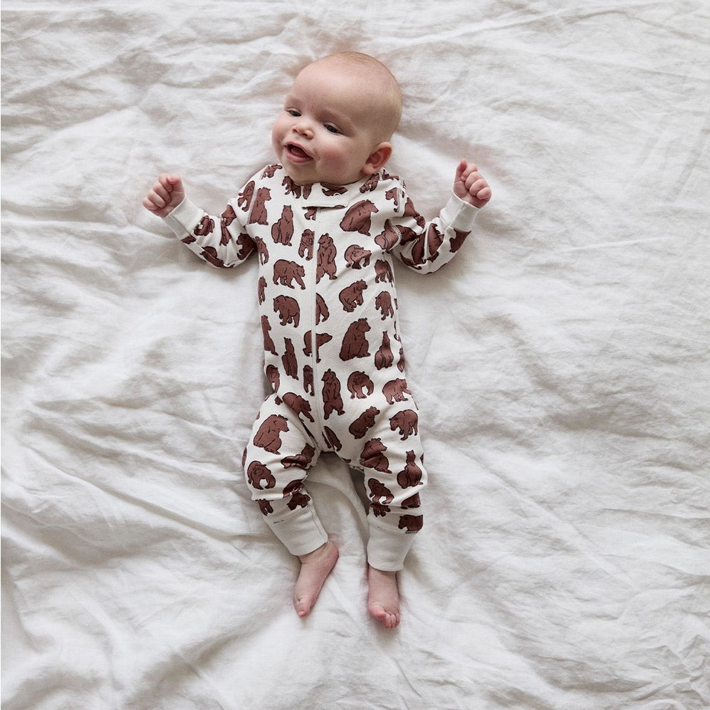 Baby wearing a brown bear-patterned onesie lying on a white textured surface