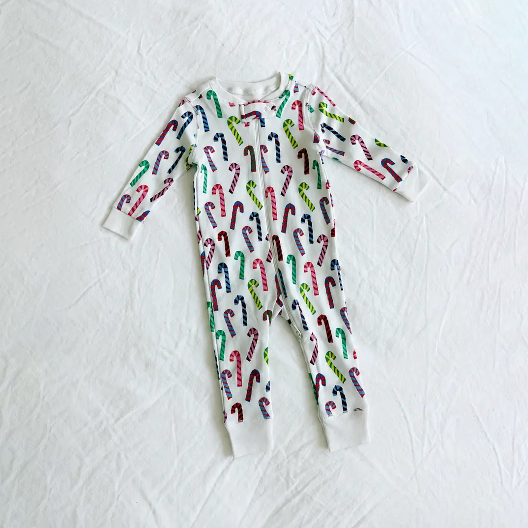 A baby long-sleeve footless one-piece pajama with an all-over candy cane print, laid flat on a white fabric background.