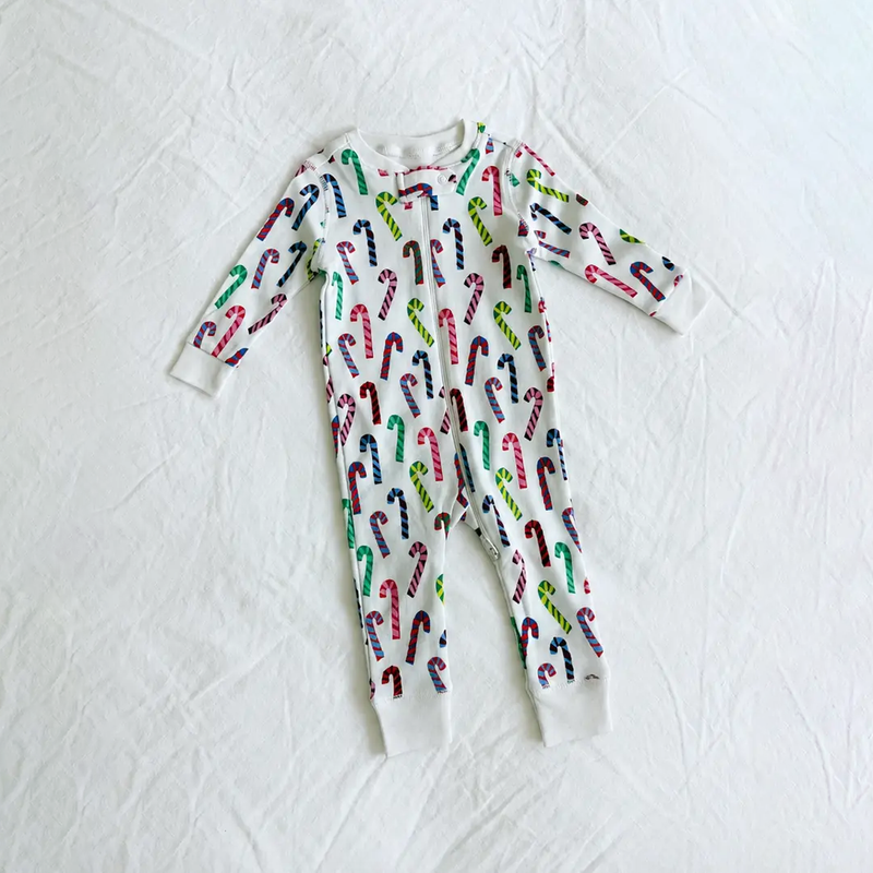 A baby long-sleeve footless one-piece pajama with an all-over candy cane print, laid flat on a white fabric background.