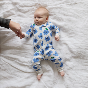 Baby wearing a blue floral onesie lying on a white bed