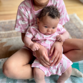 Two children in matching pink outfits sitting on a rug.