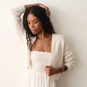 Woman wearing a white dress and cardigan against a plain background
