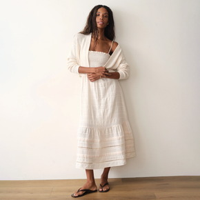 Woman wearing a white dress with a matching cardigan against a plain background
