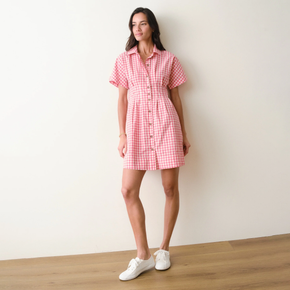 Woman wearing a red and white checkered dress standing against a plain wall.