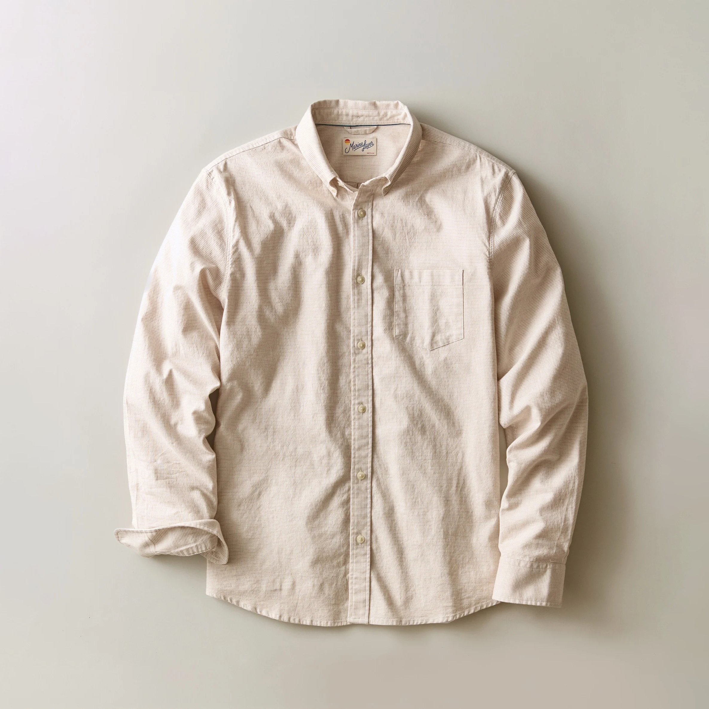 A light beige long-sleeve button-down shirt with a single chest pocket, laid flat against a neutral light gray background.
