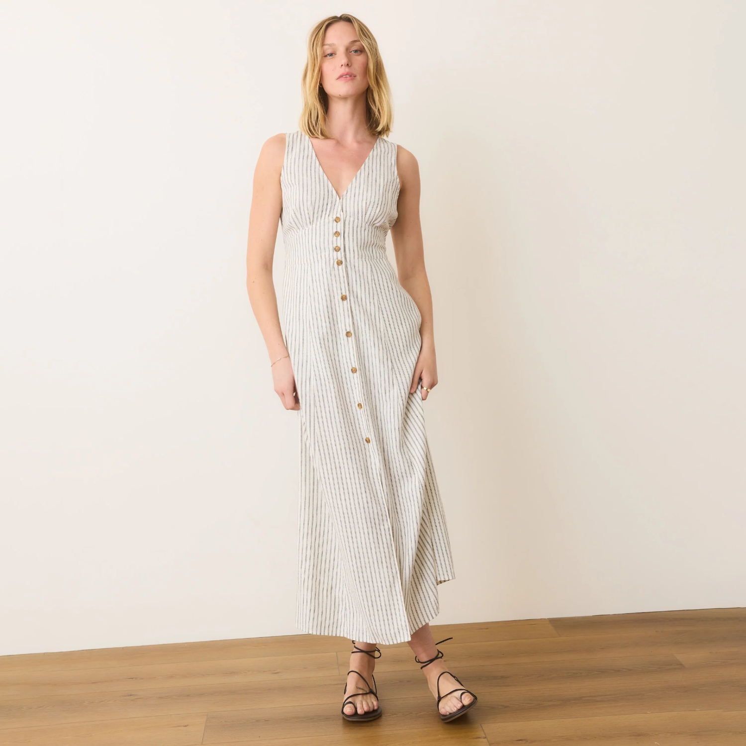 Woman wearing a white and gray striped dress with buttons on a plain background