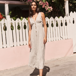 Woman in a long dress standing in front of a white picket fence with pineapple designs.