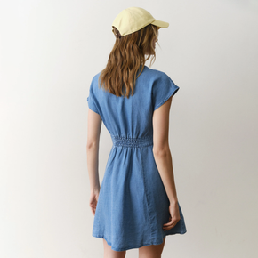 Woman wearing a blue dress and yellow cap from behind on a plain background