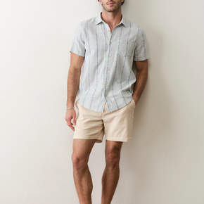 Man wearing a light blue striped shirt and beige shorts against a plain background