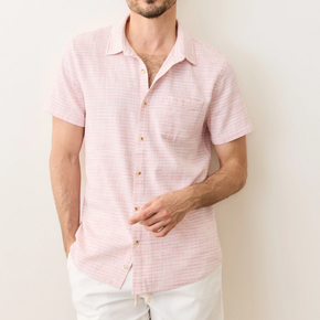 Man wearing a pink short-sleeve shirt and white shorts against a plain background