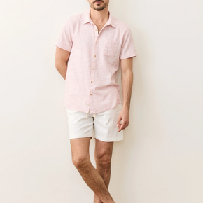 Man wearing a light pink shirt and white shorts against a plain background
